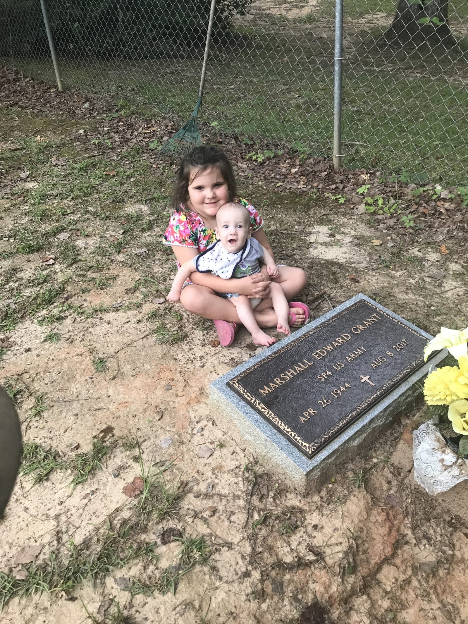 A child holding a baby beside a family memorial marker